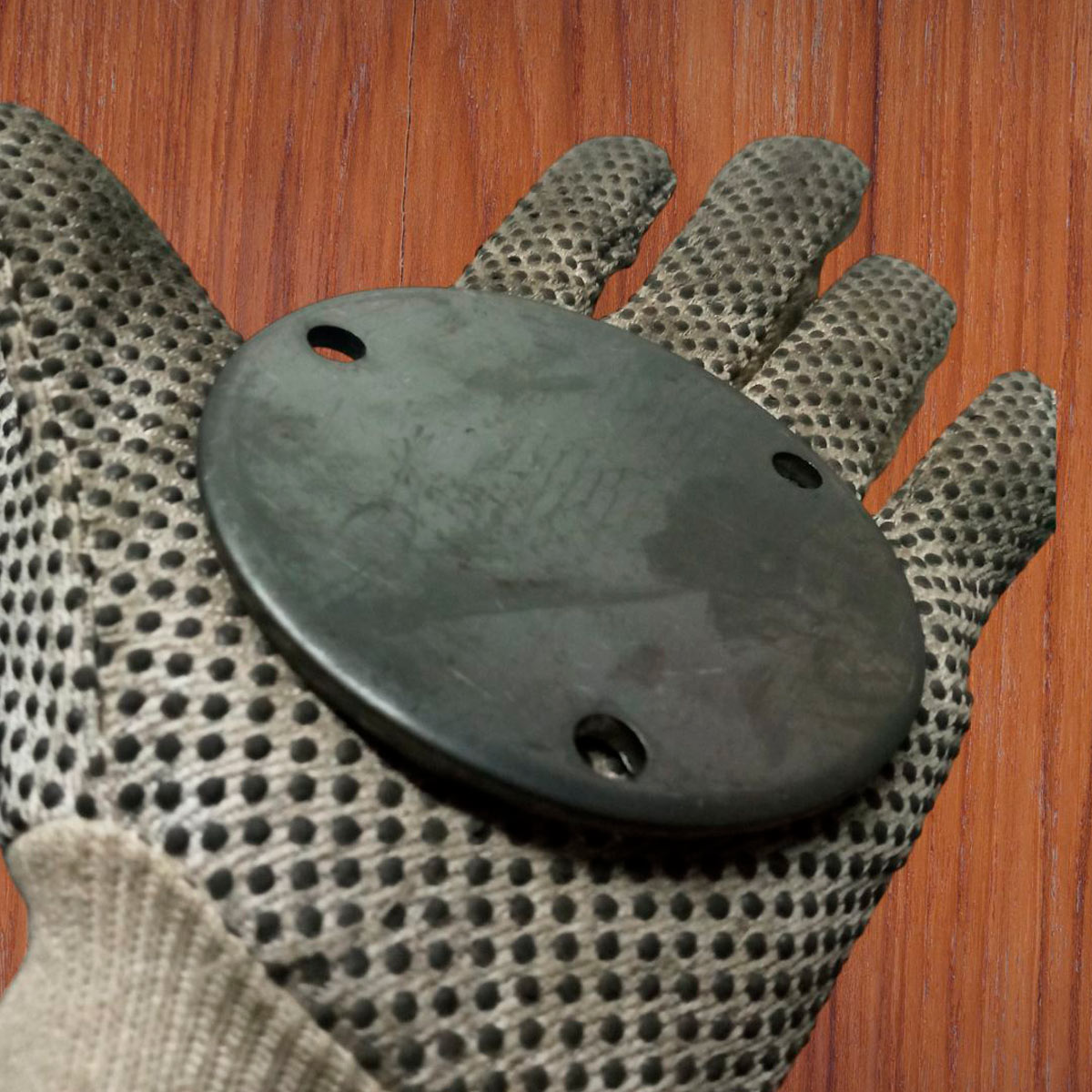 En la imagen una mano con guantes sosteniendo una base de anclaje redonda de 100x4mm con sus huecos.