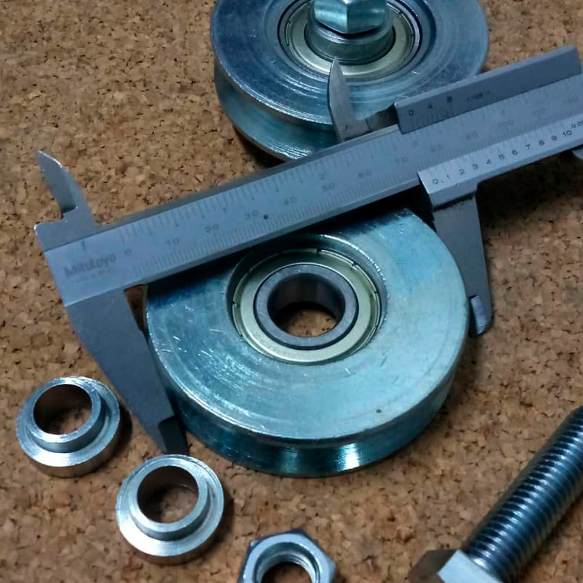 Vista de una roldana de 3" canal en V siendo medida con un vernier y al lado sus accesorios y otra rueda.