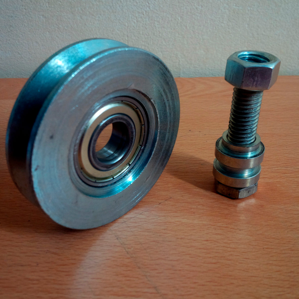Rueda para portones livianos de 2 1/2" canal en V con su tornillo, separadores y tuerca sobre un piso de madera.